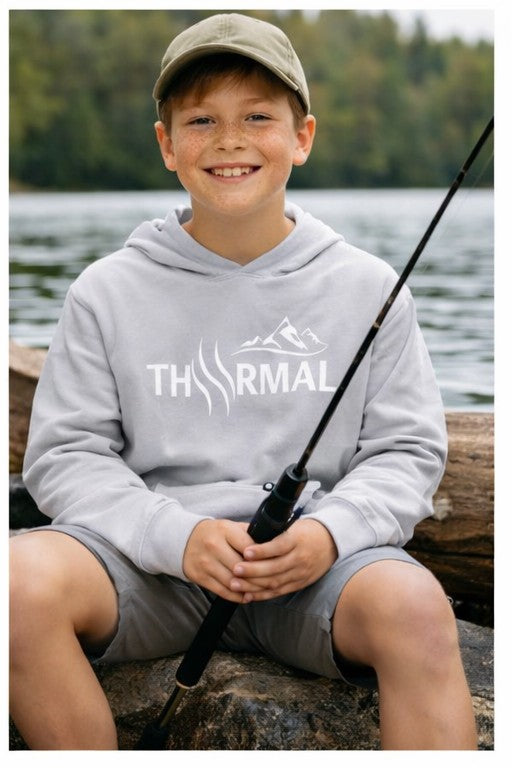 Child wearing a hoodie with 'THRMAL' branding, holding a fishing rod by a body of water.